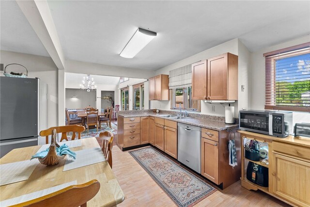kitchen featuring appliances with stainless steel finishes, a sink, light wood-style floors, a chandelier, and a peninsula