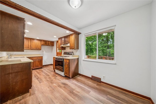161 Reaghard Dr, West Deer, PA 15024 - kitchen featuring white gas range, under cabinet range hood, brown cabinetry, a sink, and baseboards