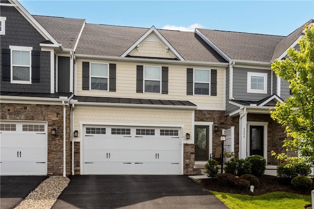 view of property with stone siding, driveway, an attached garage, a standing seam roof, and a shingled roof