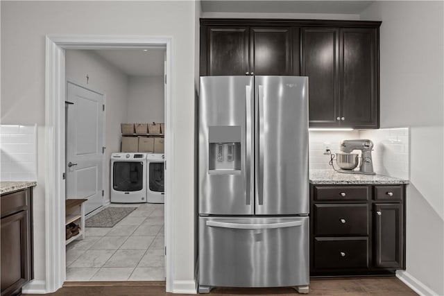 kitchen featuring stainless steel refrigerator with ice dispenser, washing machine and dryer, decorative backsplash, light stone countertops, and dark brown cabinets