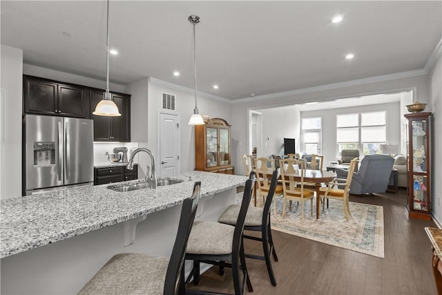 kitchen with stainless steel fridge, a sink, crown molding, light stone countertops, and dark wood finished floors