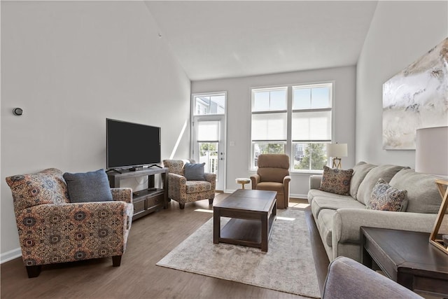 living area with plenty of natural light, wood finished floors, baseboards, and high vaulted ceiling