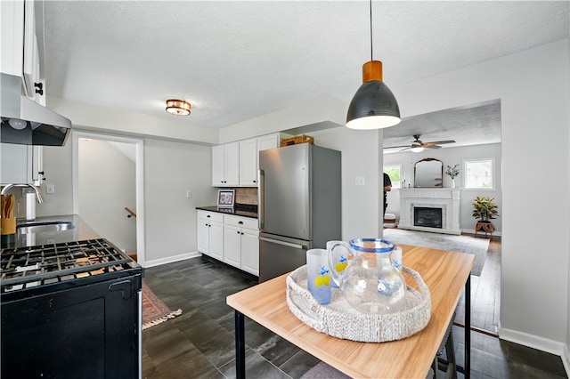 kitchen with a sink, freestanding refrigerator, under cabinet range hood, a ceiling fan, and a textured ceiling