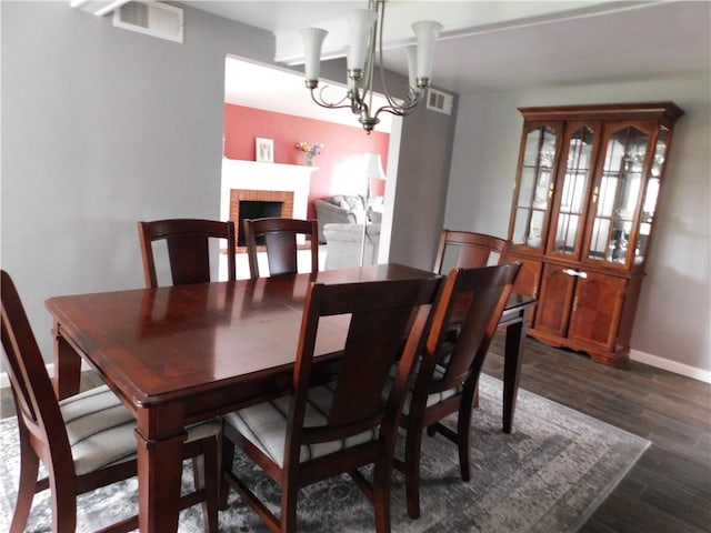 dining area featuring dark wood finished floors, baseboards, a chandelier, and a brick fireplace