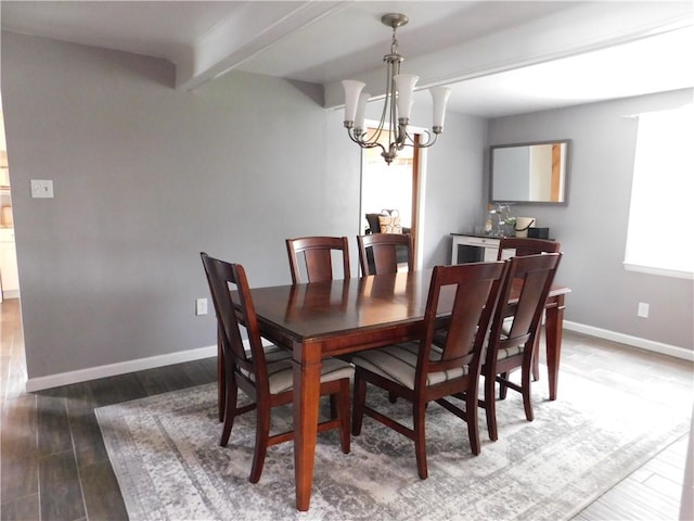 dining space featuring a chandelier, wood finished floors, baseboards, and beam ceiling