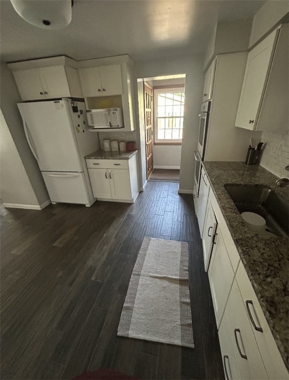 kitchen with white appliances, a sink, baseboards, and white cabinets