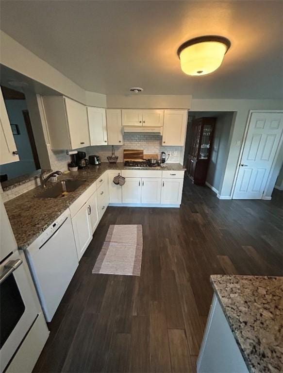 kitchen with white dishwasher, a sink, stone counters, white cabinetry, and oven