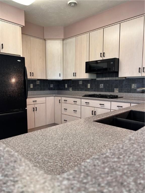 kitchen featuring black appliances, tasteful backsplash, light stone countertops, and a sink