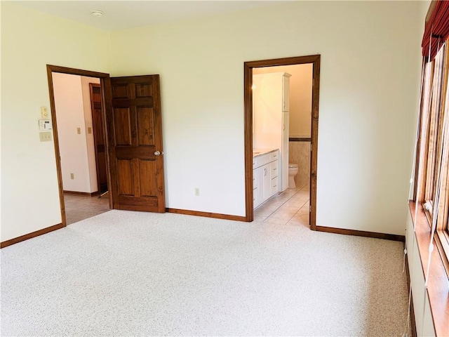 unfurnished bedroom with light carpet, baseboards, and ensuite bathroom
