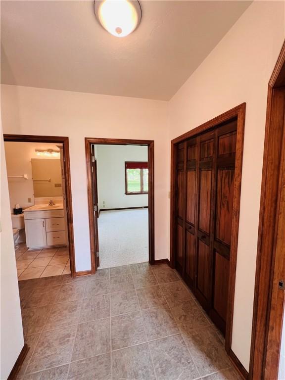 hall featuring a sink, light tile patterned floors, baseboards, and light colored carpet