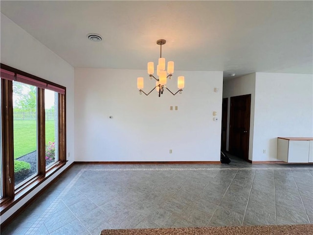 tiled empty room featuring a chandelier and baseboards