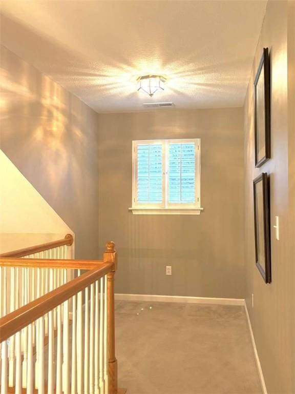 hallway featuring baseboards, a textured ceiling, and an upstairs landing