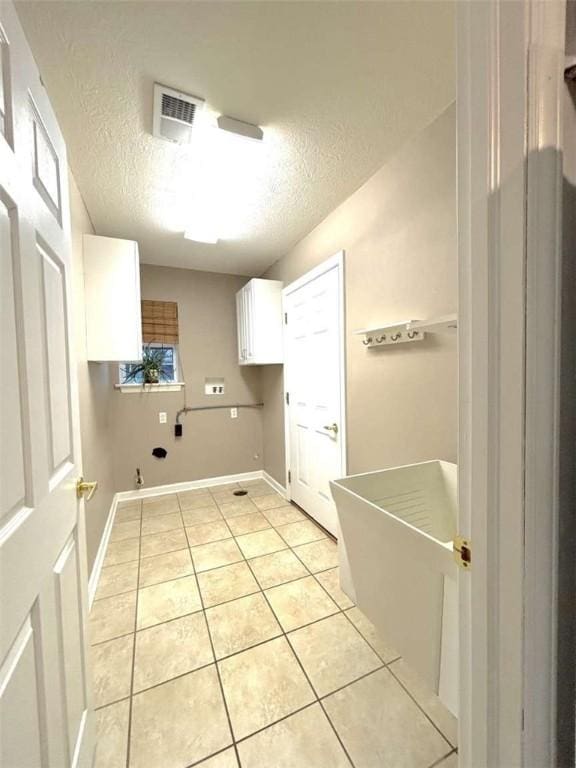 clothes washing area with cabinet space, a textured ceiling, light tile patterned flooring, hookup for a gas dryer, and baseboards