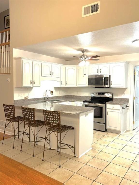 kitchen with stainless steel appliances, a peninsula, a sink, a breakfast bar, and white cabinetry