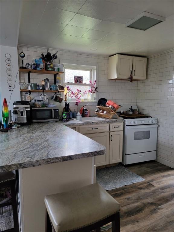 301 Main St, E Mahoning/Marion Ctr, PA 15759 - kitchen with white gas stove, a sink, stainless steel microwave, a breakfast bar, and dark wood-style flooring