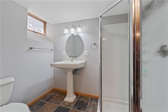 bathroom featuring baseboards, stone tile flooring, toilet, and a stall shower