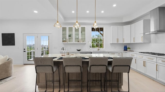 130 Prospect St, Mt Washington, PA 15211 - kitchen featuring wall chimney range hood, light wood-type flooring, white cabinetry, a kitchen island with sink, and recessed lighting