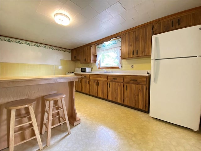 35 Kenmore Rd, West Salem Twp, PA 16125 - kitchen with white appliances, a breakfast bar area, light floors, light countertops, and brown cabinets