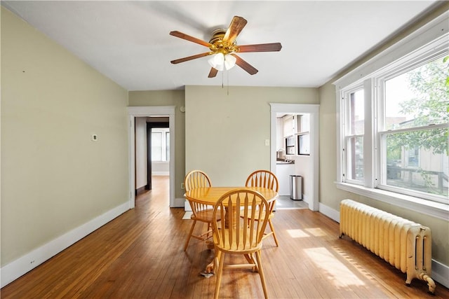 dining area with radiator heating unit, wood-type flooring, baseboards, and a ceiling fan