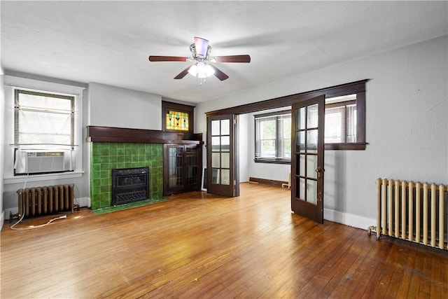 unfurnished living room featuring radiator, a tiled fireplace, hardwood / wood-style flooring, and a ceiling fan