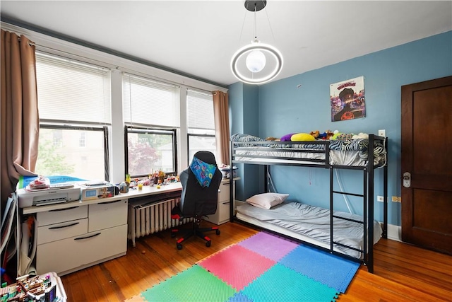 bedroom with wood finished floors, an office area, and radiator heating unit