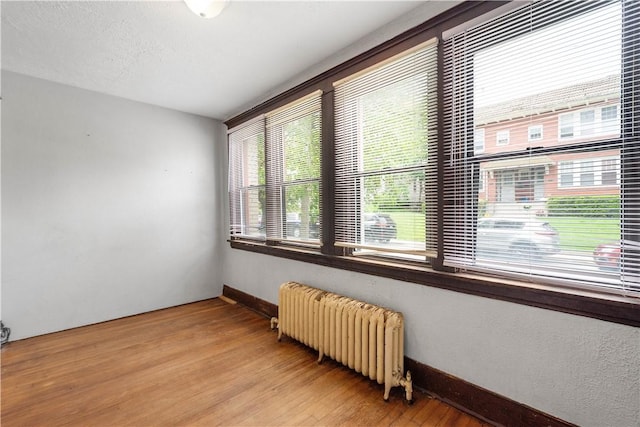 unfurnished room featuring radiator, light wood-style flooring, and baseboards