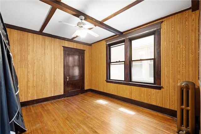 unfurnished room featuring radiator, wood walls, hardwood / wood-style flooring, baseboards, and beam ceiling