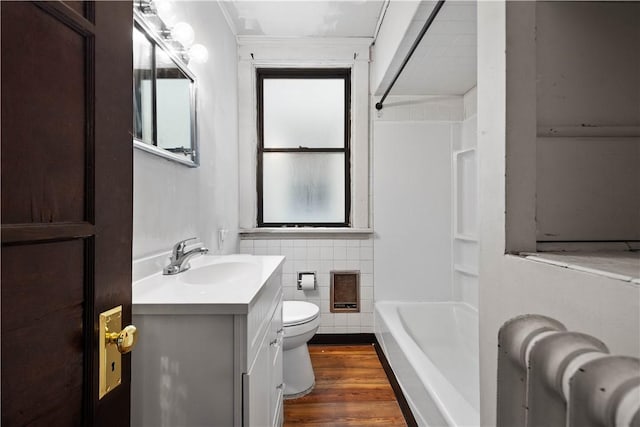 bathroom with toilet, vanity, wood finished floors,  shower combination, and ornamental molding