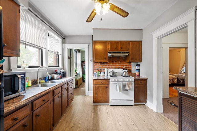 kitchen with white gas range oven, under cabinet range hood, stainless steel microwave, a sink, and light wood-style floors