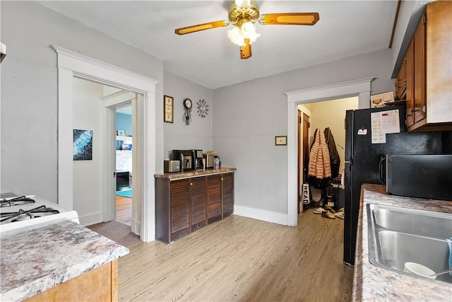 kitchen with light wood-style floors, a ceiling fan, brown cabinetry, baseboards, and a sink