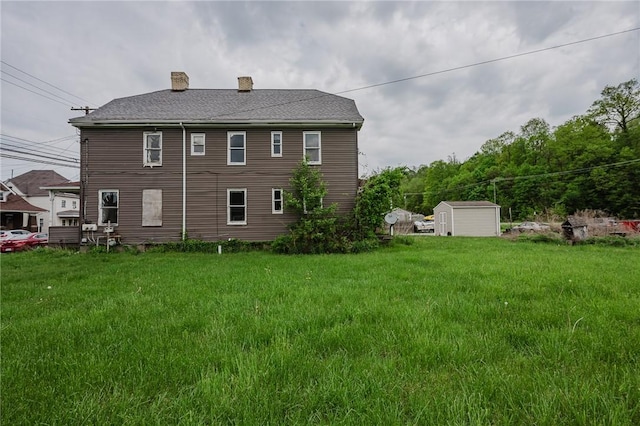 back of property with a shed, a chimney, an outbuilding, and a yard