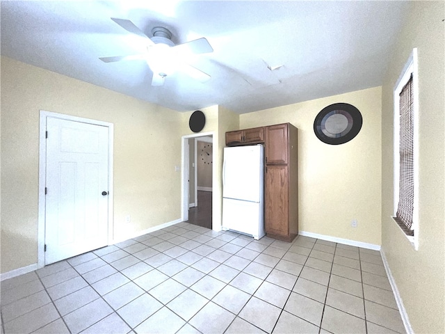 empty room featuring a ceiling fan, light tile patterned flooring, and baseboards