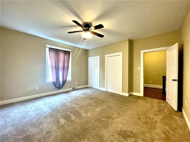 unfurnished bedroom with two closets, carpet, baseboards, and ceiling fan