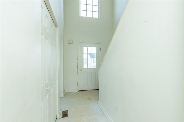 doorway featuring plenty of natural light, baseboards, a high ceiling, and light floors