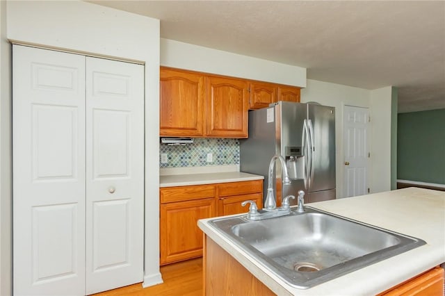 kitchen featuring stainless steel fridge, a sink, brown cabinets, light countertops, and backsplash