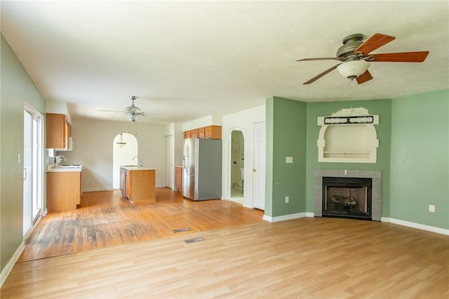 unfurnished living room with ceiling fan, light wood-style flooring, a sink, and baseboards