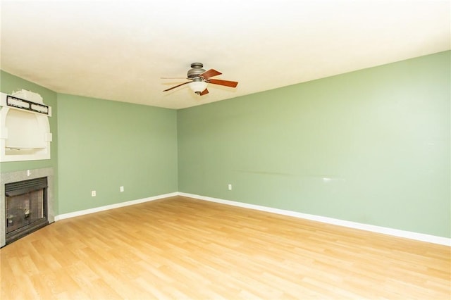 unfurnished living room with light wood-style flooring, a ceiling fan, a fireplace, and baseboards