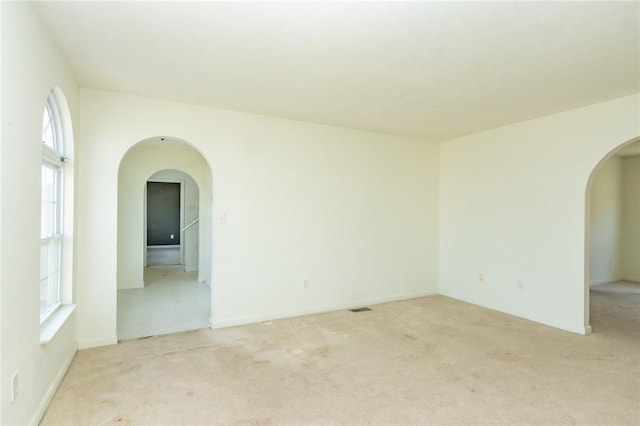 spare room featuring arched walkways, light colored carpet, and plenty of natural light