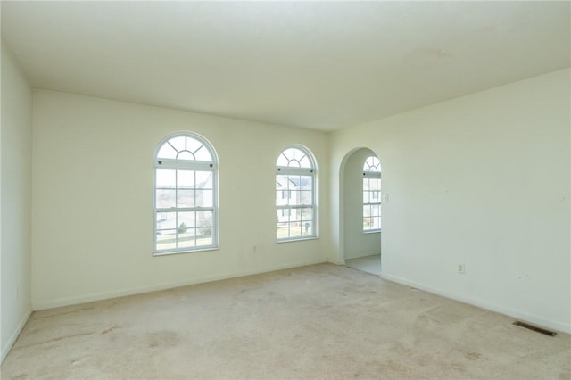 spare room featuring healthy amount of natural light, carpet floors, and arched walkways