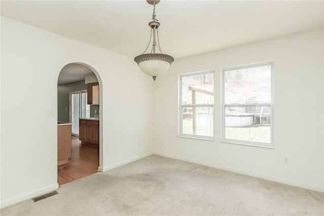 spare room featuring light carpet, arched walkways, plenty of natural light, and baseboards