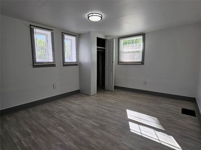 unfurnished bedroom with wood finished floors, multiple windows, and baseboards