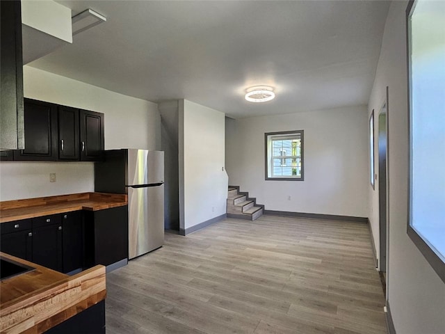 kitchen with butcher block countertops, dark cabinetry, freestanding refrigerator, and light wood finished floors