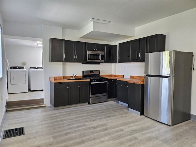 kitchen with stainless steel appliances, washer and clothes dryer, dark cabinets, and wooden counters