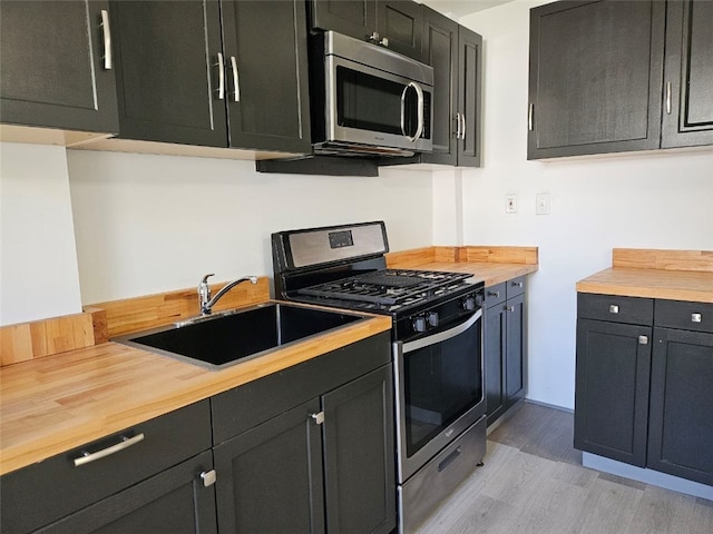 kitchen with stainless steel appliances, a sink, light wood-style floors, and butcher block countertops