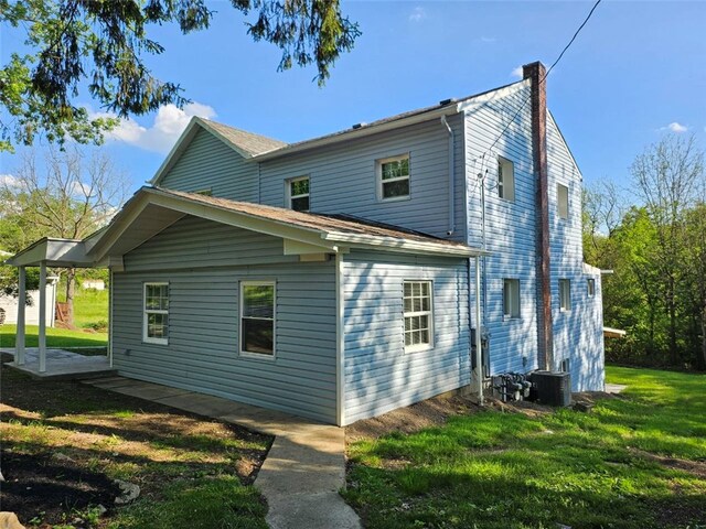 rear view of house featuring a chimney, a lawn, and cooling unit