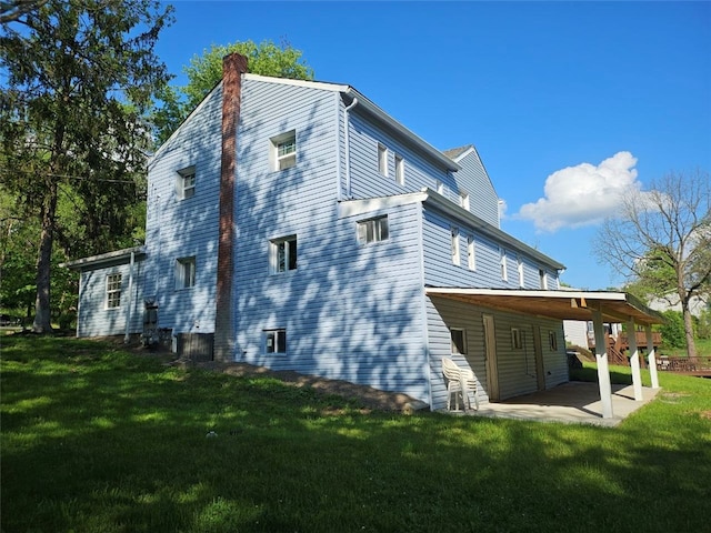back of house with a chimney, a lawn, and a patio