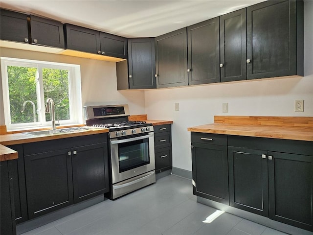 kitchen with stainless steel gas range, wood counters, a sink, and dark cabinetry