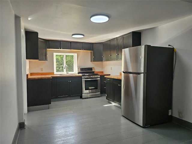 kitchen featuring stainless steel appliances, a sink, butcher block countertops, and dark cabinetry