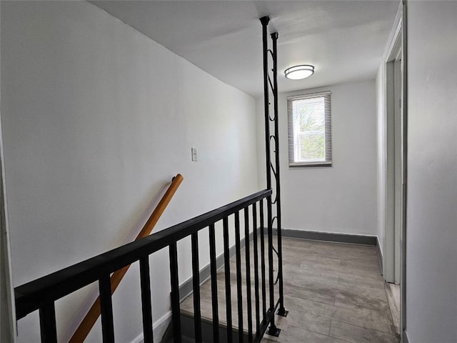 corridor featuring an upstairs landing, light wood-style floors, and baseboards