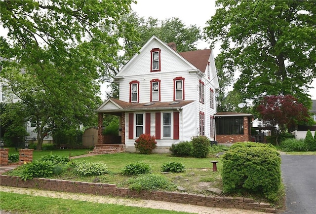 victorian-style house with a front yard, an outbuilding, a storage unit, and a sunroom